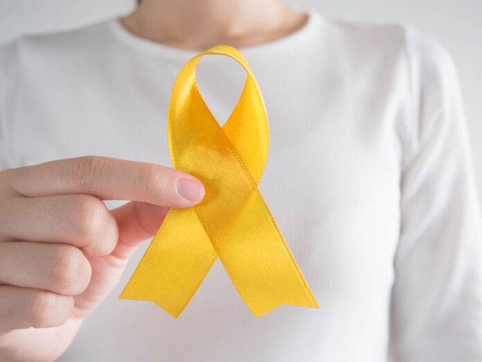 World AIDS day in December month campaign. Red ribbon awareness Young female holding yellow gold ribbon awareness symbol for endometriosis, suicide prevention, sarcoma bone cancer, bladder cancer, liver cancer and childhood cancer concept. Health care. Close up.